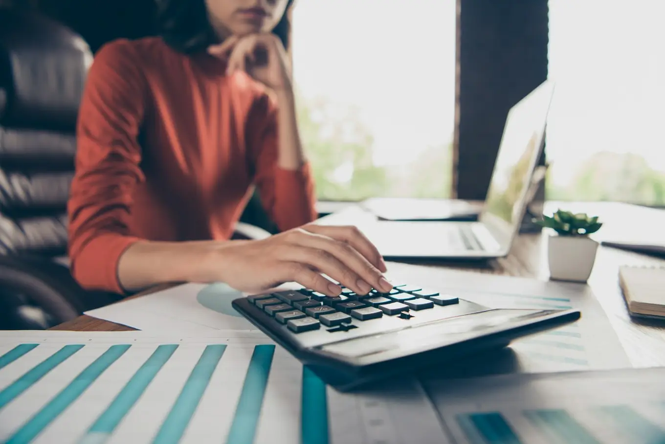 kobieta z kalkulatorem przed laptopem